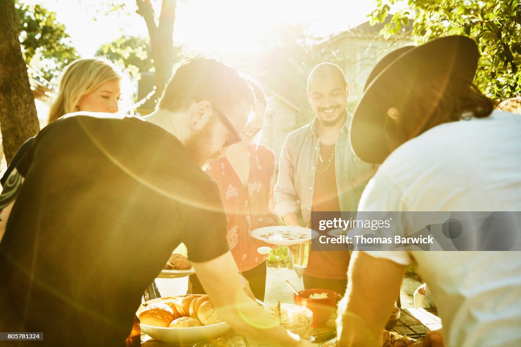 Smiling friends dishing up food in backyard on summer evening