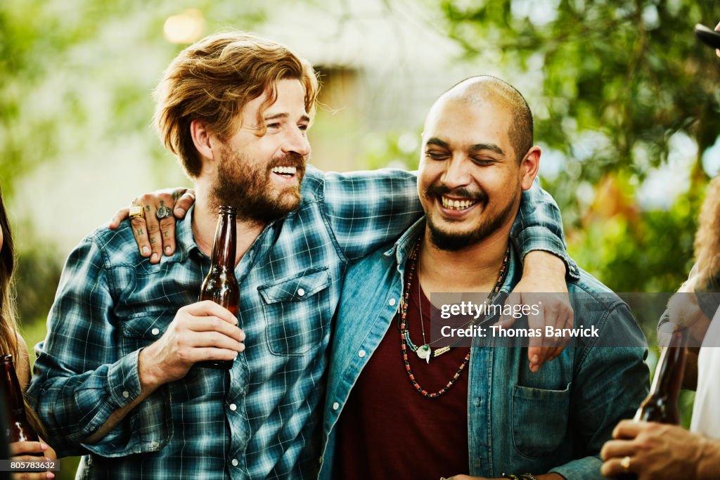 Laughing friends with arms around each others shoulders hanging out during backyard barbecue