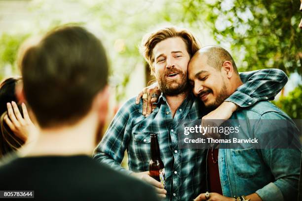 two friends embracing during backyard party on summer evening - vrienden stockfoto's en -beelden