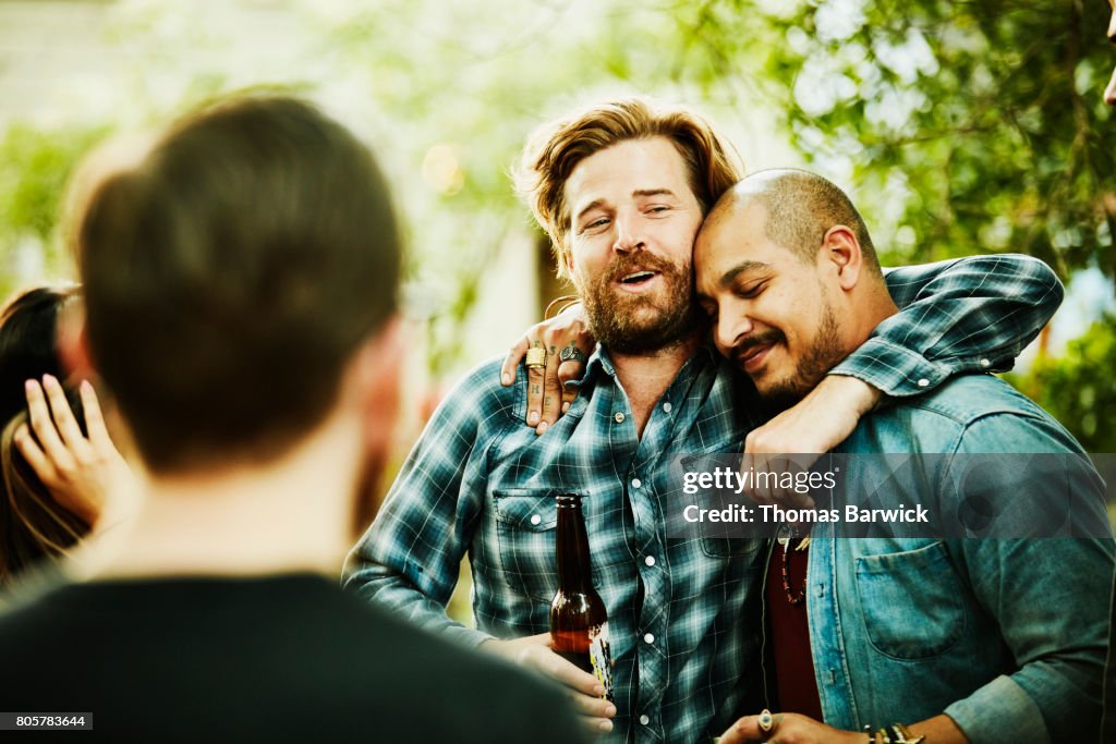 Two friends embracing during backyard party on summer evening
