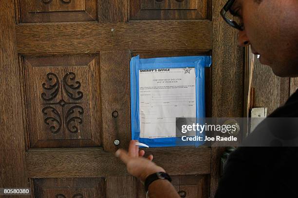 Jim Banford from Real Estate Asset Disposition corp. Looks at the Sheriffs eviction notice posted on the front door of the foreclosed property his...