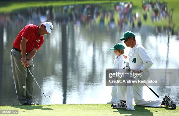 Phil Mickelson putts as his son Evan and caddie Jim "Bones" McKay look on during the Par 3 Contest prior to the start of the 2008 Masters Tournament...