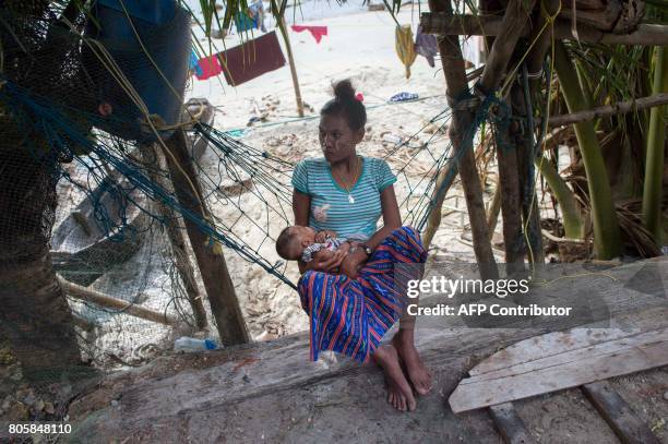 This picture taken on May 13, 2017 shows a member of the Moken tribe holding a child as she sits in front of her home near the coast in Makyone Galet...
