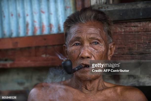 This picture taken on May 13, 2017 shows Kar Shar, the Moken leader smoking his pipe as he sits in front of his home in Makyone Galet village in the...