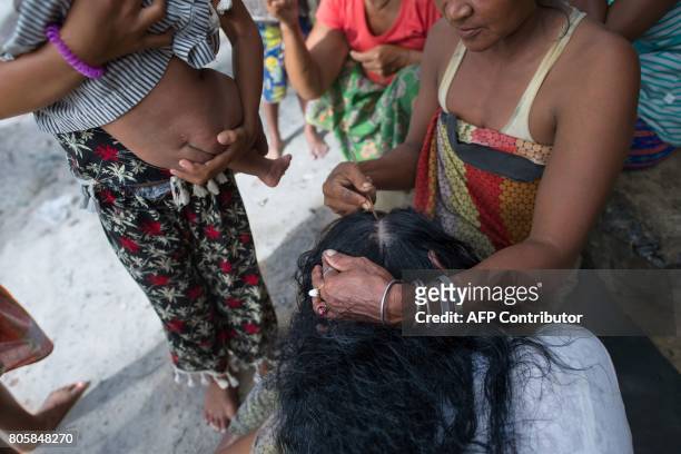 This picture taken on May 13, 2017 shows female members of the Moken tribe fixing their hair and taking care of children in front of one of their...