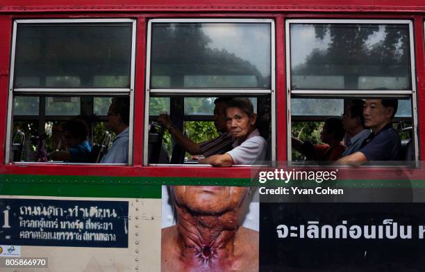 Passenger in a public bus in Bangkok peers out of a window above a particularly gruesome and shocking anti-smoking advertisement. In recent years the...