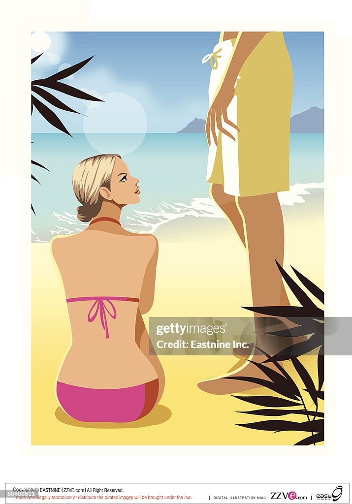 Rear view of a woman sitting on the beach with a man standing beside her