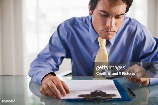 businessman with magnifying glass reading small print - petits caractères photos et images de collection