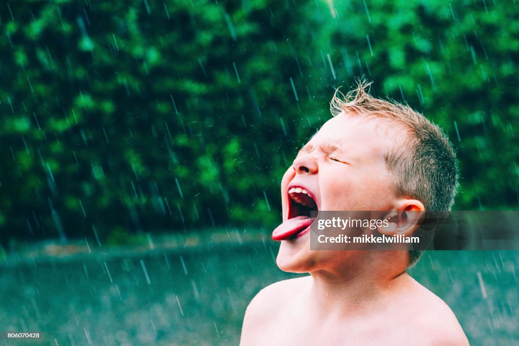 Zomerregen giet en jongen smaakt de regendruppels