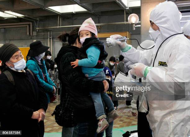 An official in a full radiation protection suit scans an evacuated mother and child with a geiger counter to check radiation levels in Koriyama city...