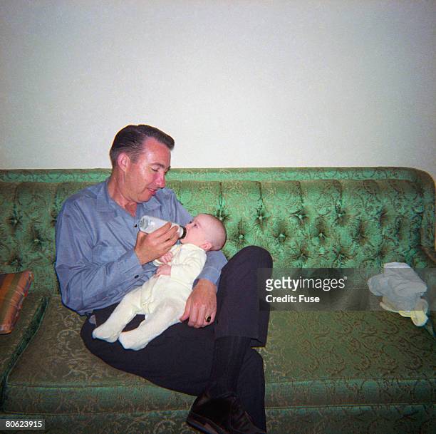 father bottle-feeding baby on sofa - 1950s father stock pictures, royalty-free photos & images