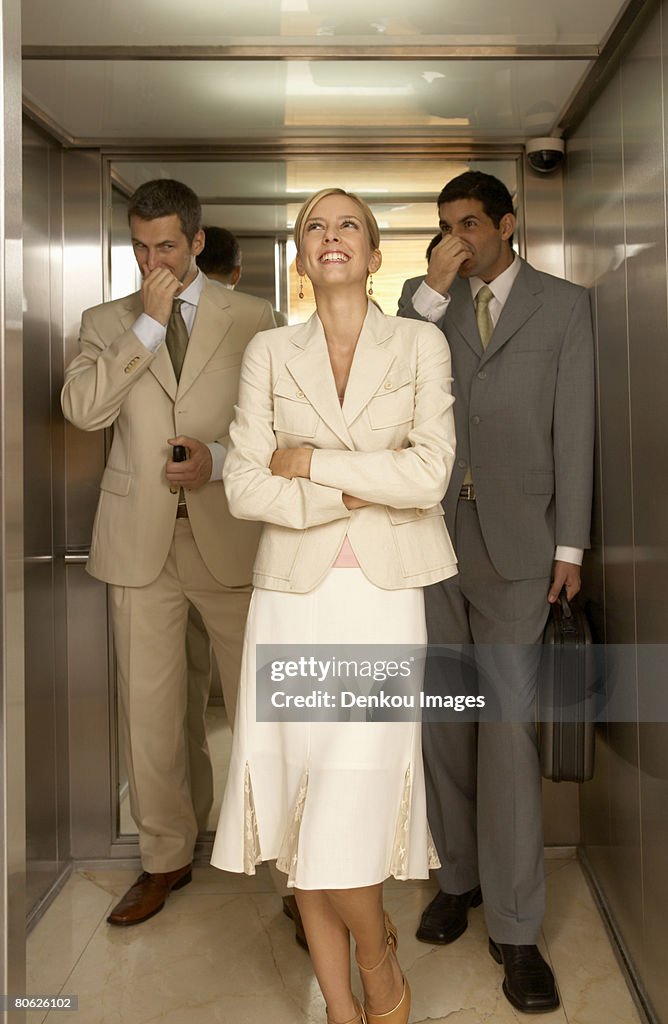 Businesswoman with two businessmen holding their noses in an elevator