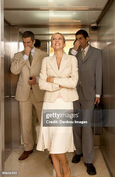 businesswoman with two businessmen holding their noses in an elevator - onaangename geur stockfoto's en -beelden