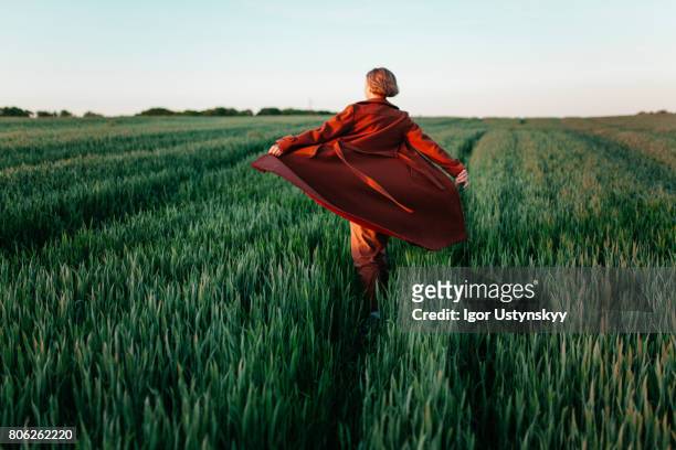 woman in red coat  walking  in the field at sunset - fashion for peace stockfoto's en -beelden