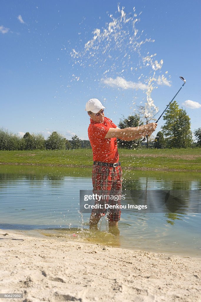 Side profile of a mid adult man swinging a golf club in waterhole in a golf course