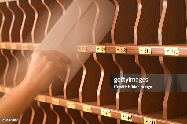 hand putting letters into pigeon holes at hotel reception - pigeon hole stock pictures, royalty-free photos & images