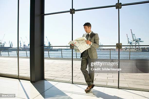 full body portrait of businessman reading newspaper in front of window - man standing full body photos et images de collection