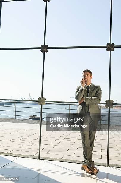 full body portrait of businessman talking on mobile phone in front of window - man standing full body photos et images de collection