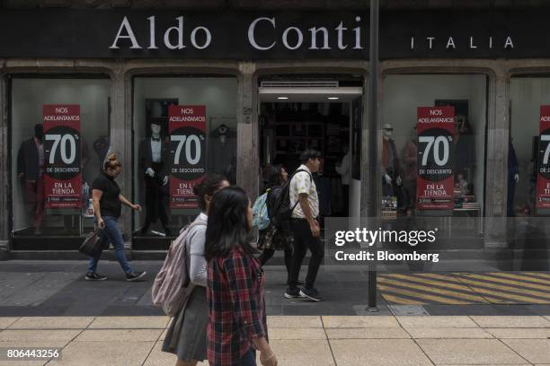 Pedestrians pass in front of sale signs displayed in the window of an Aldo Conti clothing store on Francisco I. Madero Avenue in Mexico City, Mexico,...