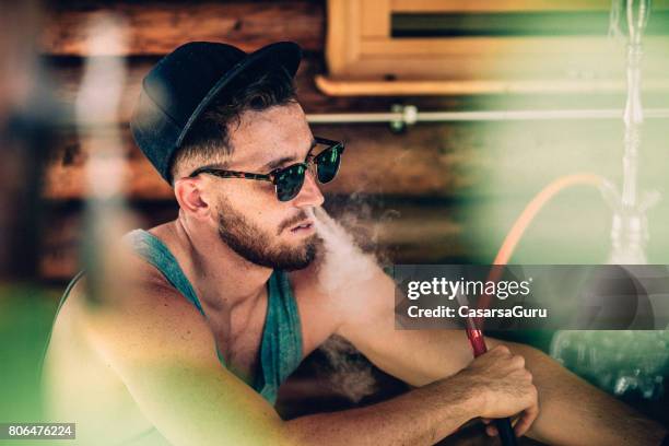 young adult man smoking hookah and exhaling smoke through nose - hookah stock pictures, royalty-free photos & images