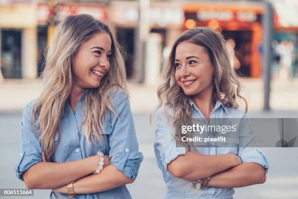 zusters met gekruiste armen kijken naar elkaar - adult twins stockfoto's en -beelden