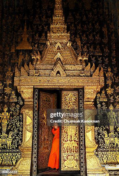 Laos Buddhist monk stands in front of temple at Wat Xieng Thong during the Songkran festival on April 13 in Luang Prabang, Laos. The Songkran...
