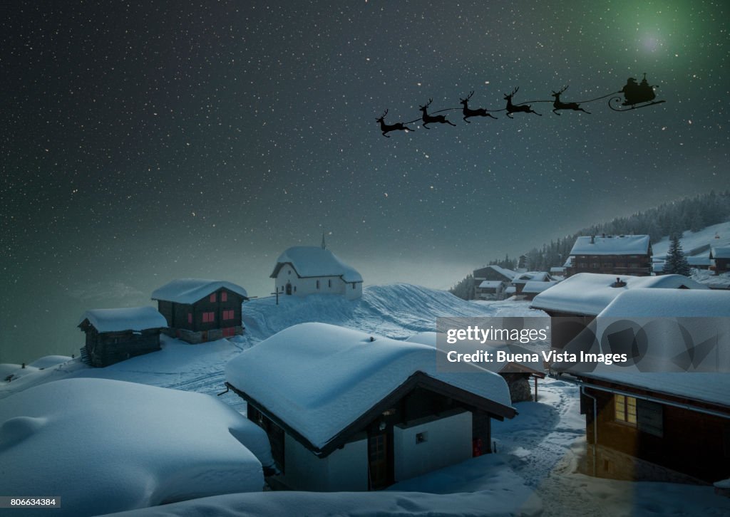 Santa's sledge in a starry sky over a village in the snow