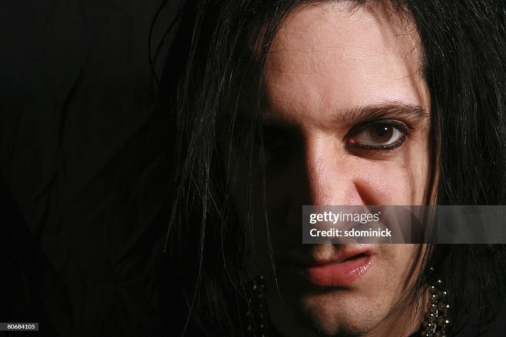 A goth style man with a sneer on his face.