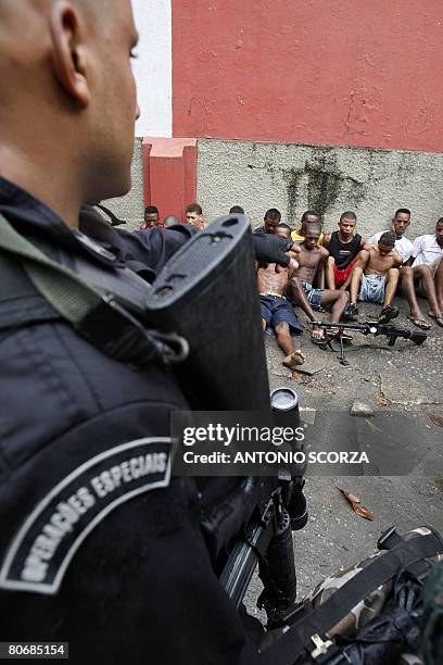 Special Police Operations Battalion member guards some of the 14 residents of Vila Cruzeiro shantytown arrested under suspicion of being members of...