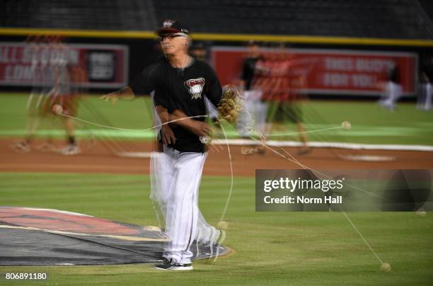 Multiple exposure of first base coach Dave McKay of the Arizona Diamondbacks uses a ball on a string to warm his arm up prior to throwing batting...