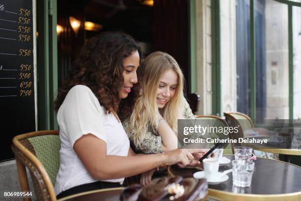 2 young women to the terrace of a parisian coffee - women smartphone city paris stock pictures, royalty-free photos & images