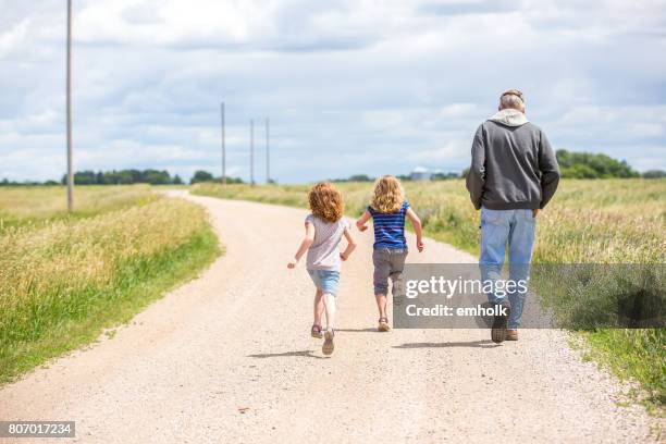 chicas y abuelo caminando y acabando el camino de grava rural - región central de eeuu fotografías e imágenes de stock
