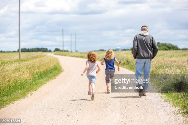 girls & grandpa walking & running out rural gravel driveway - scena rurale foto e immagini stock