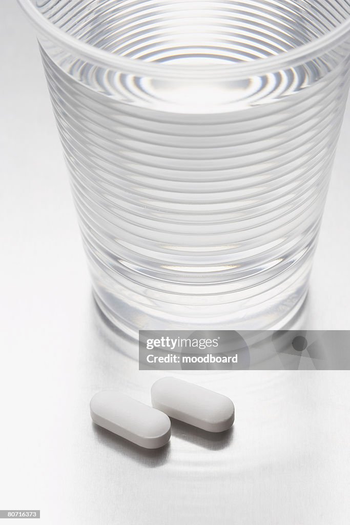 Two pills beside water in plastic cup