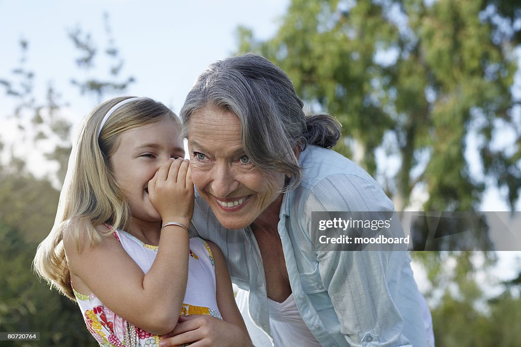 Granddaughter (5-6) whispering to grandmother's ear outdoors