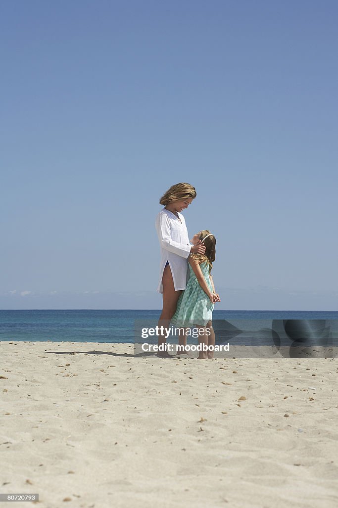 Mother and daughter (5-6) standing face to face on beach