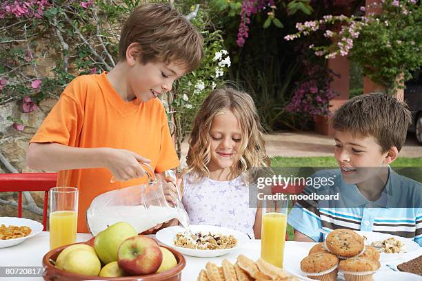 two boys and girl (6-11) at table boy pouring milk on cereal garden - boy eating cereal stock pictures, royalty-free photos & images