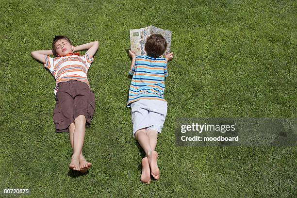 two boys (6-11) lying on grass one reading elevated view - lying on back stock pictures, royalty-free photos & images