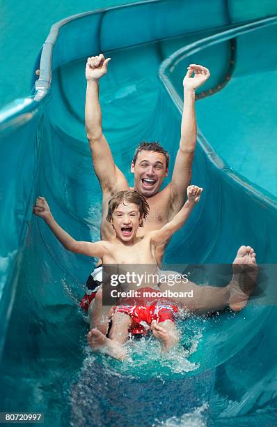 father and son (7-9) with arms outstretched on water slide - water slide stockfoto's en -beelden