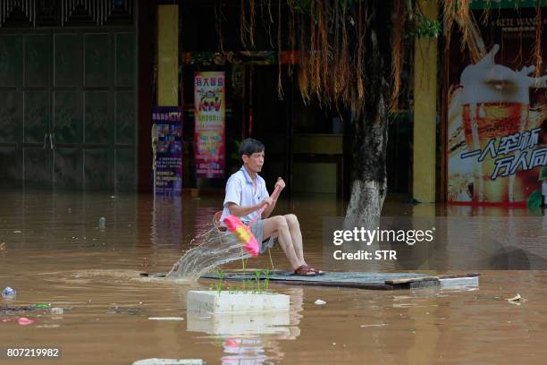 This picture taken on July 3, 2017 shows a man using an improvised flotation device to move through floodwaters on a flooded street in Liuzhou,...