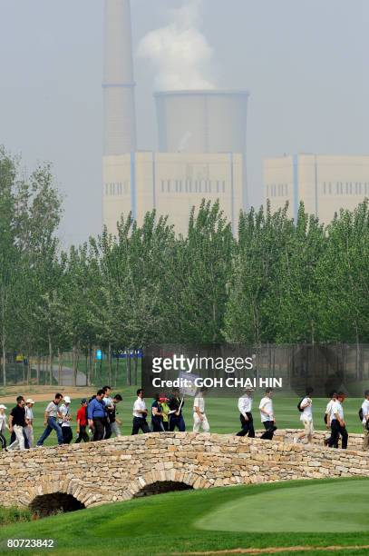 Spectators and golfers make their way across a bridge on the Beijing CBD International Golf Club with the background of a power station cooling...