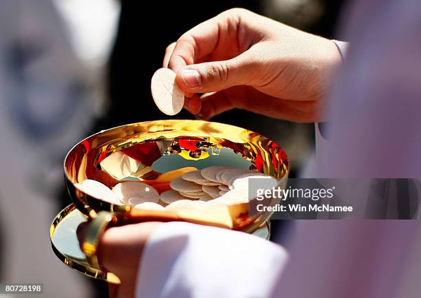 Priest holds a Holy Communion wafer as Pope Benedict XVI celebrates Mass at Nationals Park April 17, 2008 in Washington, DC. Today is Pope Benedict...