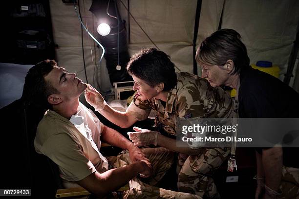 British Army nurses Capt. Lindsay Baigent and Captain Anne Stavelyon clean a British soldier's face wound, from a non combat incident, before...