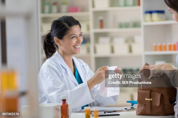young pharmacist hands customer a bag of prescription medication - prescription drugs dangers stock pictures, royalty-free photos & images