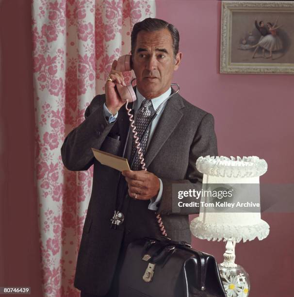 An unidentified doctor holds a notebook as he makes a telephone call from a pink decor room, mid to late twentieth century.