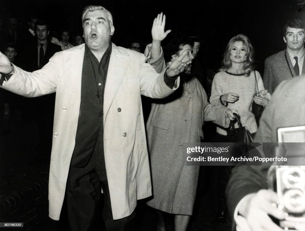 Cinema Personalities pic: 27th October 1963. French film actress Brigitte Bardot, (born 1934), pictured in London protected by an escort including arm waving film producer Ardan as disorderly crowds caused the film "Adorable Idiot" to be abandoned while