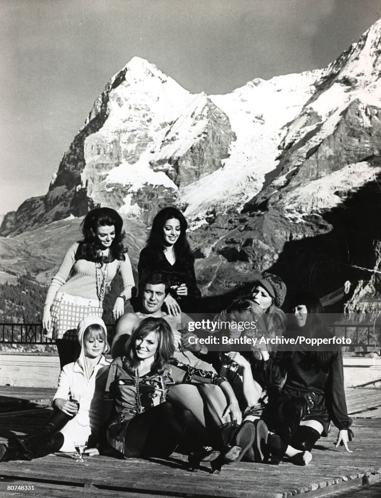 Cinema Personalities pic: 22nd October 1968. Switzerland. Actor George Lazenby in a break from filming the James Bond film "On Her Majesty's Secret Service" surrounded by glamour girls from the film with a backdrop of the Eiger. Back l-r, Helena Ronney,