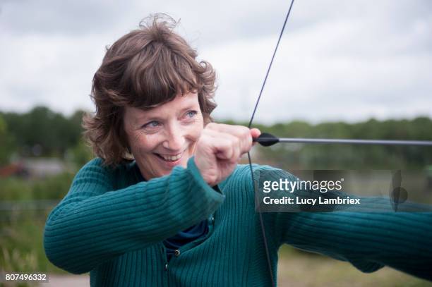 mature woman shooting bow and arrow - arco y flecha fotografías e imágenes de stock