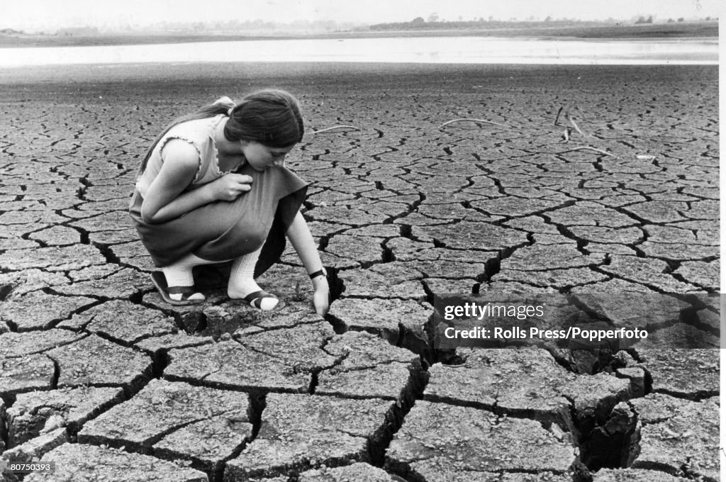 Social History Weather. Drought. Northamptonshire, England. pic: 5th July 1976. A young local girl puts her hand into the deep cracks in the dried-up Pitsford Resevoir, Northants, where the water level had dropped to danger point. The resevoir which supp