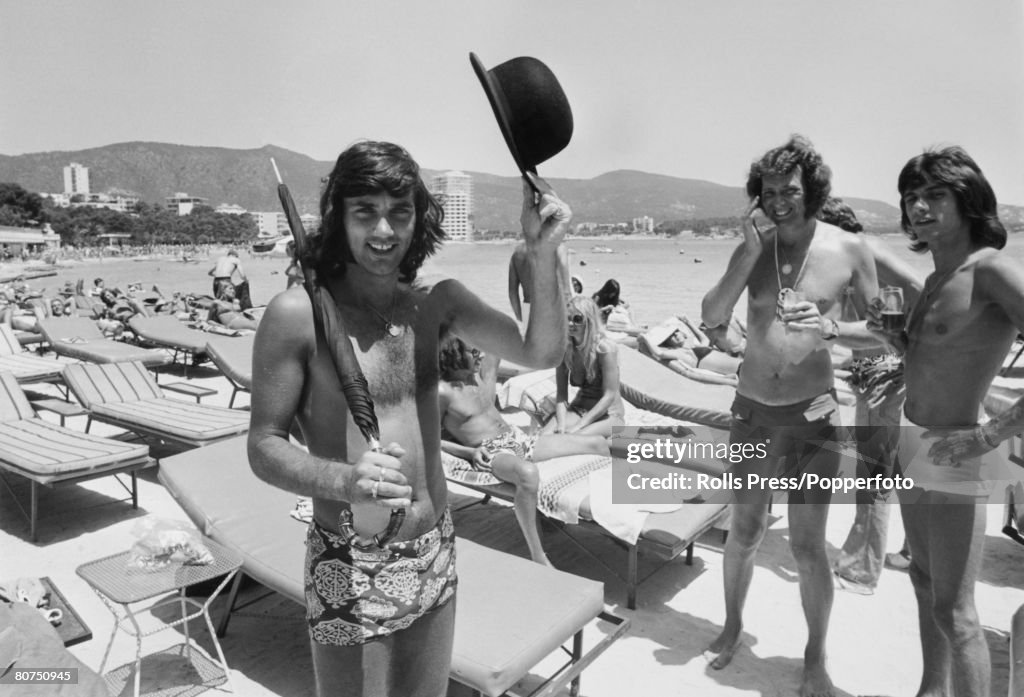 Sport Football. Majorca, Spain. 1971. Manchester United player George Best on holiday. Seen here with friends relaxing in the sun and carrying a black bowler hat and umbrella.
